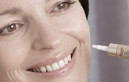 Femme appliquant un produit Eucerin sur sa joue gauche.